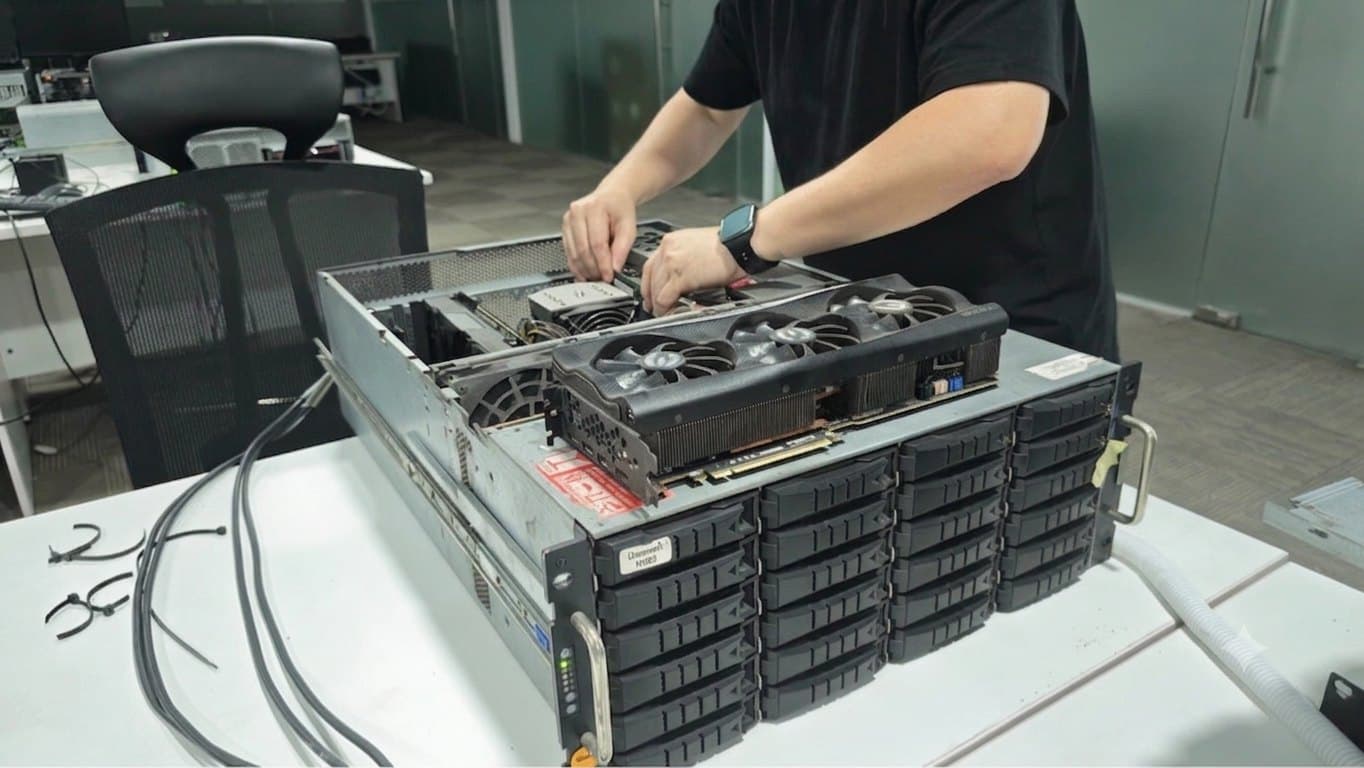 A technician seating a graphics card into an open 4U rackmount chassis on a workbench.