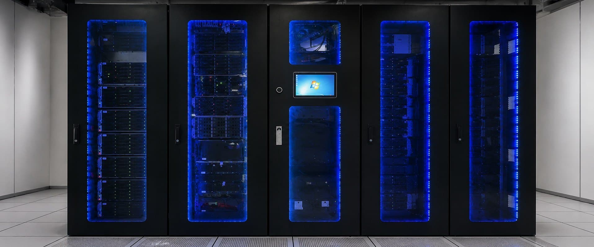 A row of black server cabinets lit from within by blue LED strips, on a raised floor.